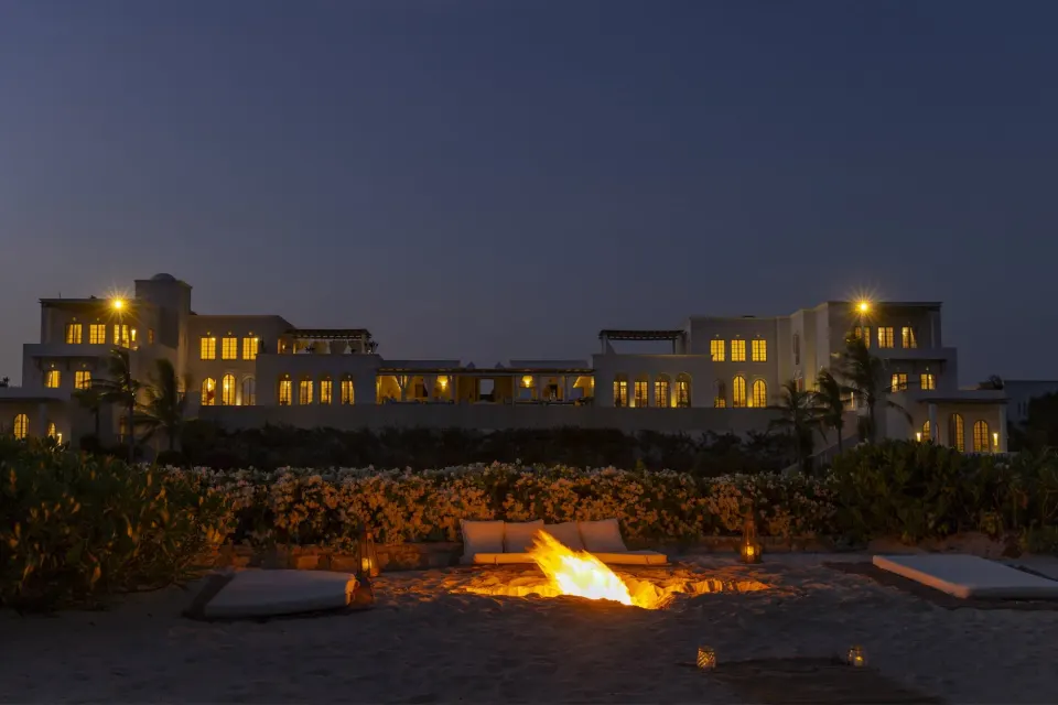 A bonfire on the beach with the villa lit up behind