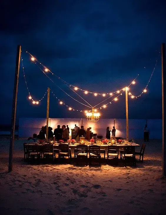 A long dinner table on the beach under strings of lights